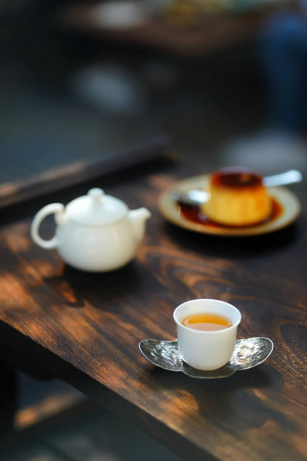 白瓷杯中的茶湯，後方是茶壺與布丁